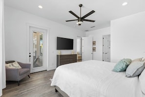 A bedroom with a bed, a ceiling fan, a dresser, and a TV mounted on the wall. - New - 3 Min To Beach - Swim Spa - Fire Pit - Games (Panama City Beach)