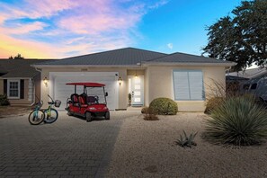 A single-story house with a garage, a red golf cart, and two bicycles parked in the driveway. - New - 3 Min To Beach - Swim Spa - Fire Pit - Games (Panama City Beach)