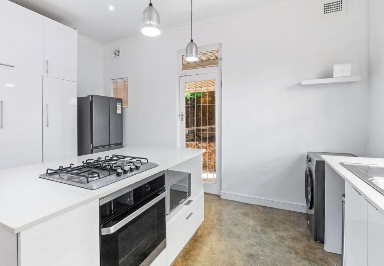 Una cocina moderna con armarios blancos, estufa a gas, horno, refrigerador y lavadora.