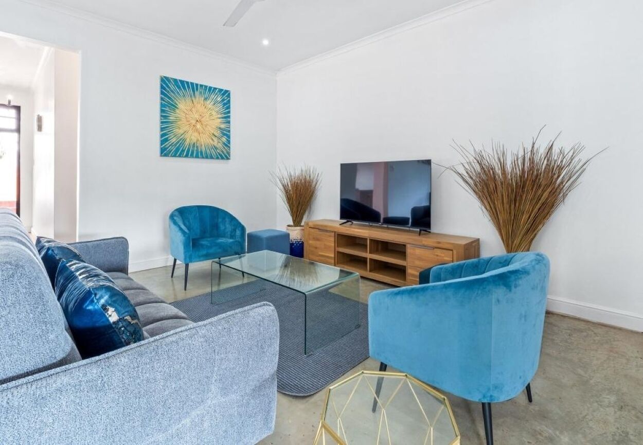 Un salón moderno con una mesa de centro de cristal, sillones de terciopelo azul, un mueble de televisión de madera y plantas decorativas.