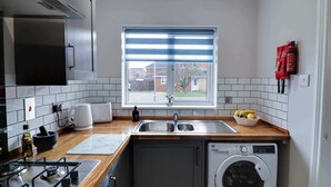 Una cocina compacta con lavadora integrada, cafetera y ventana con persianas.