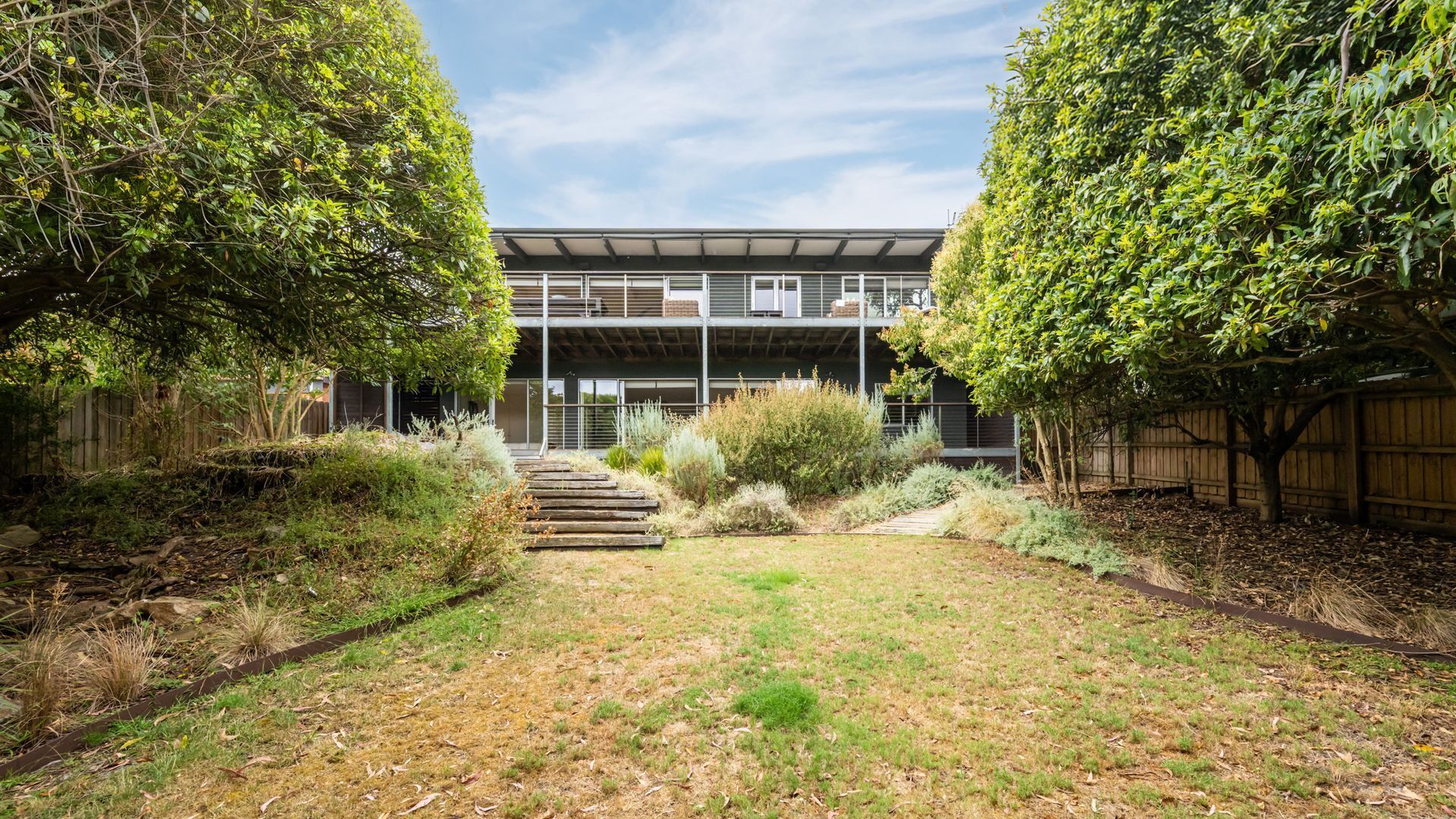 Ein modernes, zweistöckiges Haus mit einer überdachten Terrasse und einem gepflegten Garten.