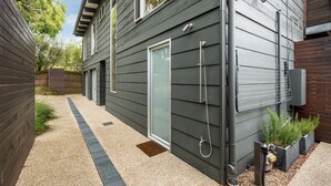 Ein modernes Haus mit dunkler Fassade, einer Schiebetür aus Glas, einem kleinen Garten mit Pflanzen und einem Kiesweg.