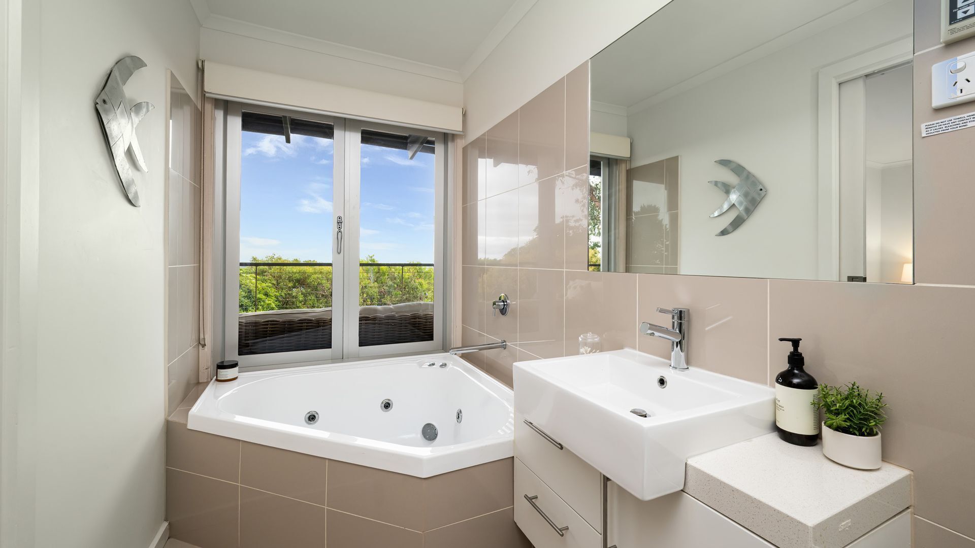 Een moderne badkamer met een ruime badkuip, twee wastafels, een spiegel en uitzicht op groen.