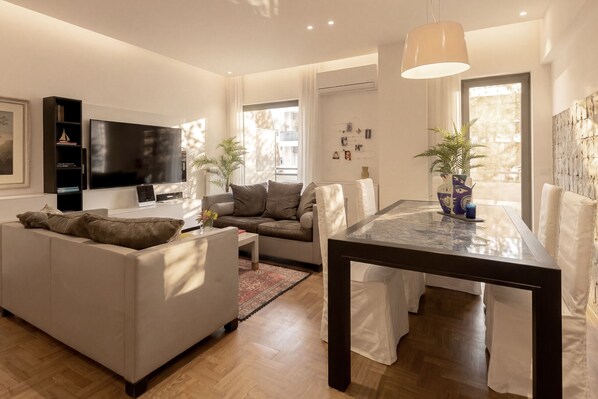 A modern living room with a sofa, a dining table, a TV, and a potted plant. - Nikita 1 3rd·Signature Athenian Residence (Athens)
