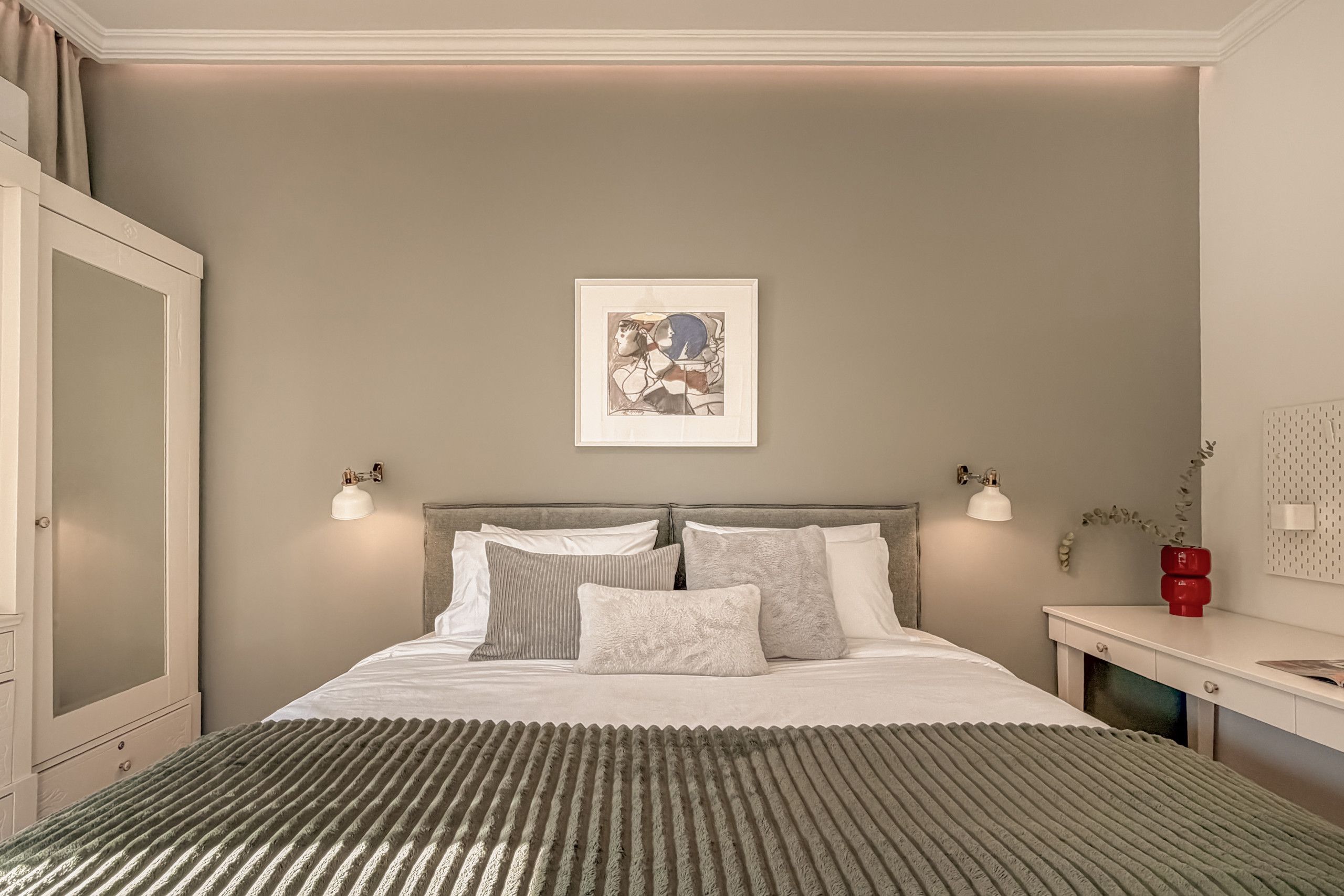 A bedroom with a bed, bedside lamps, a framed artwork, and a dresser.