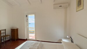 A bedroom with a bed, a chair, a wooden cabinet, a door leading to a balcony, and an air conditioning unit.