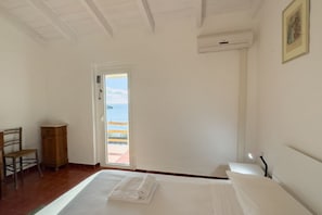 A bedroom with a bed, a chair, a wooden cabinet, a door leading to a balcony, and an air conditioning unit.