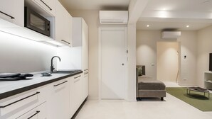 A modern kitchen with white cabinets, a microwave, and a sink. There is a bed with a green rug and a bedside table. - Palazzo Accademia-brunelleschi-1 (Florence)