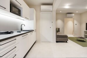 A modern kitchen with white cabinets, a microwave, and a sink. There is a bed with a green rug and a bedside table. - Palazzo Accademia-brunelleschi-1 (Florence)