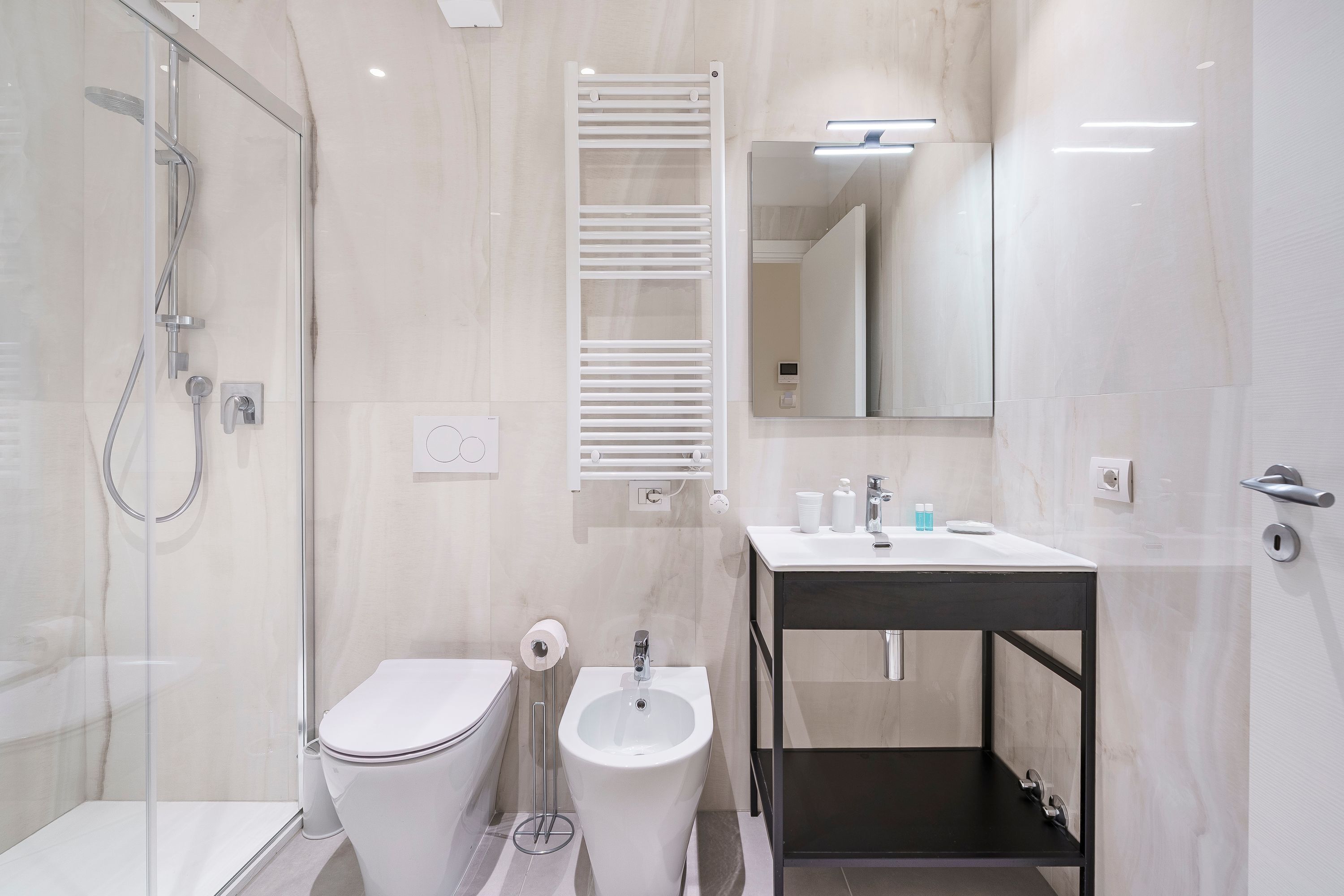 A modern bathroom with a glass-enclosed shower, a white toilet, a bidet, and a black vanity with a mirror.