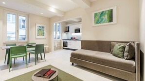 A modern living room with a sofa, chairs, a dining table, and a kitchen in the background. - Palazzo Accademia-brunelleschi-1 (Florence)