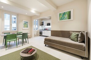 A modern living room with a sofa, chairs, a dining table, and a kitchen in the background. - Palazzo Accademia-brunelleschi-1 (Florence)