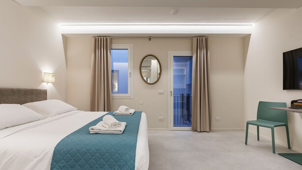 A hotel room with a bed, a desk, a chair, a TV, and a balcony door. - Palazzo Accademia-brunelleschi-1 (Florence)