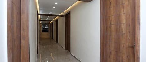 A hallway with wooden doors and a polished floor, leading to a room with a window.