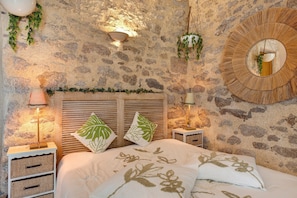 Ein Schlafzimmer mit Steinsandsteinwänden, einem Bett, zwei Wandlampen und einem runden Spiegel.