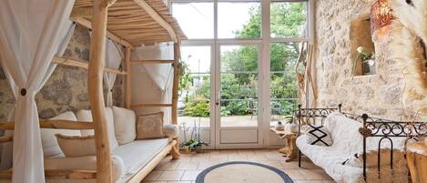 Una habitación rústica con pared de piedra, cama de madera, sofá blanco y un ventanal grande.