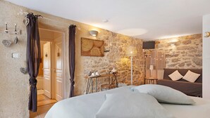 Un dormitorio con pared de piedra, una cama con almohadas, una mesita de noche con lámpara y un televisor.