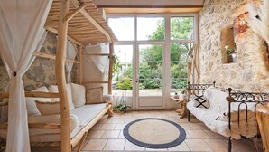A rustic room with a stone wall, a wooden bed, a white sofa, and a large window. - Bed and Breakfast 'Chambre Bohème' with Shared Garden and Wi-Fi (Saint-Malô-du-Bois)