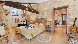 A rustic bedroom with a wooden ceiling, a bed with a beige bedspread, a guitar, and a dining area with a table and chairs. - Bed and Breakfast 'Chambre Bohème' with Shared Garden and Wi-Fi (Saint-Malô-du-Bois)