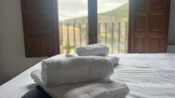 A bed with neatly folded white towels and a view of a balcony with closed doors.