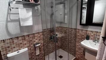 A bathroom with a glass-enclosed shower, a white toilet, a sink, and a mirror.