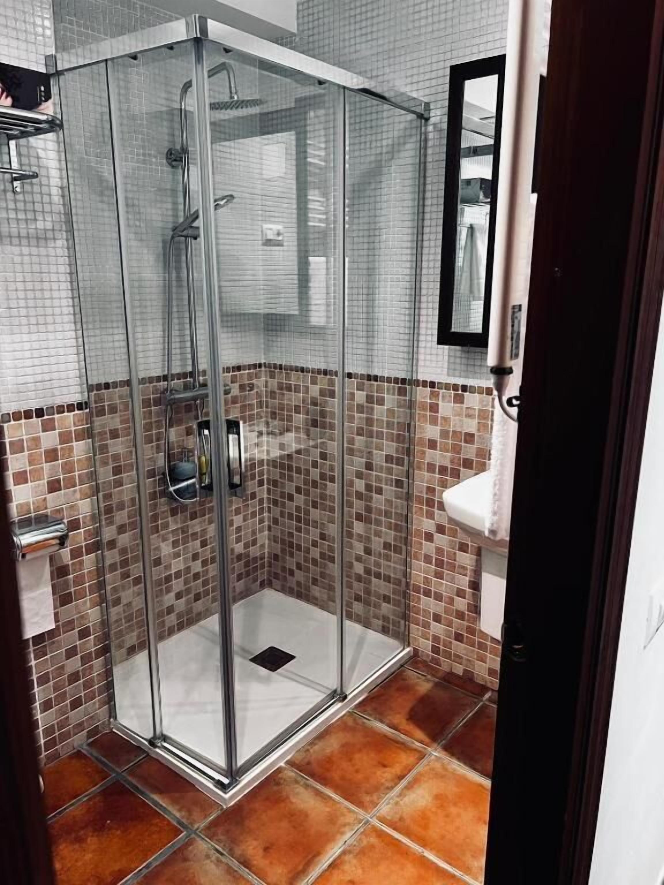 A glass-enclosed shower with a tiled floor and a white sink.