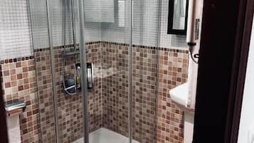 A glass-enclosed shower with a tiled floor and a white sink.