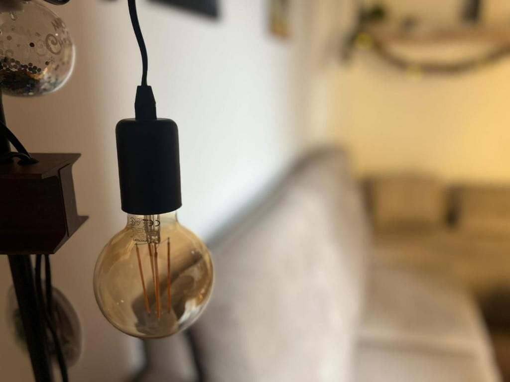 Primer plano de una bombilla con filamento visible y base negra, conectada a un cable de alimentación.