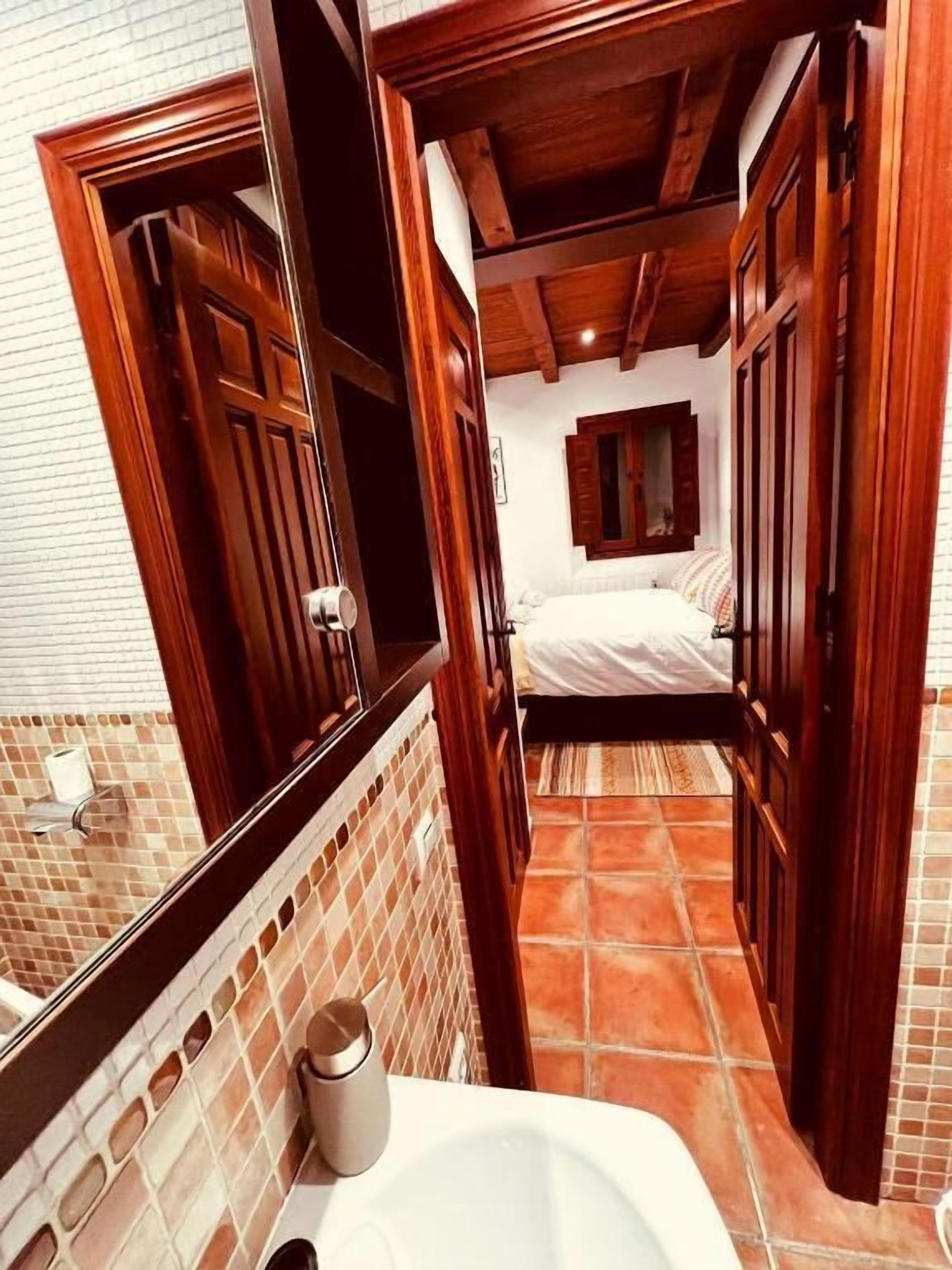 Un baño estrecho con una puerta de madera, un lavabo blanco y un espejo.
