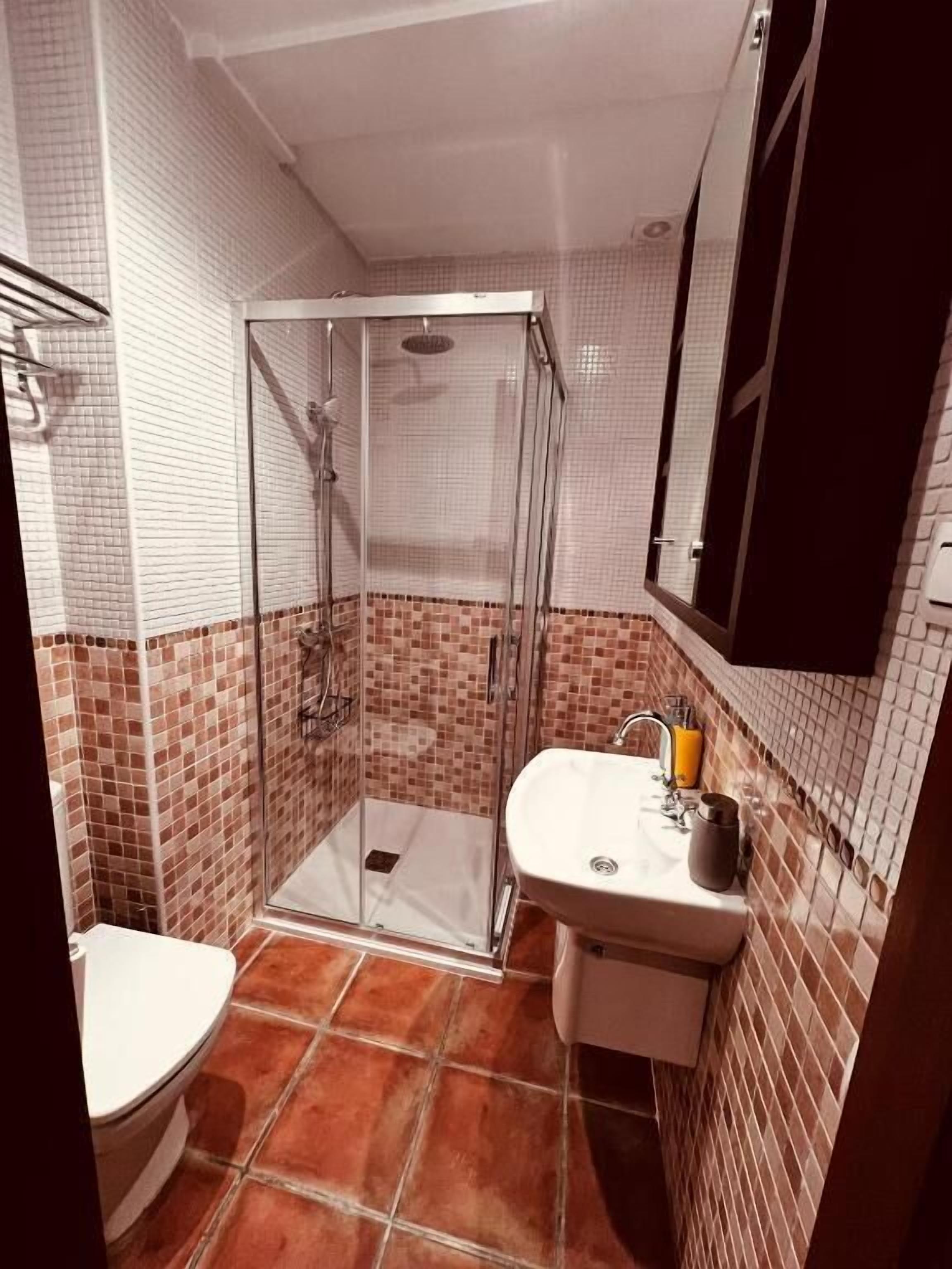 Ett badrum med en dusch som är avskärmad med glasväggar, ett vitt handfat och en toalett.