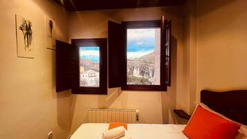 Un dormitorio con una cama, un cojín rojo y dos ventanas que dan a un paisaje montañoso.