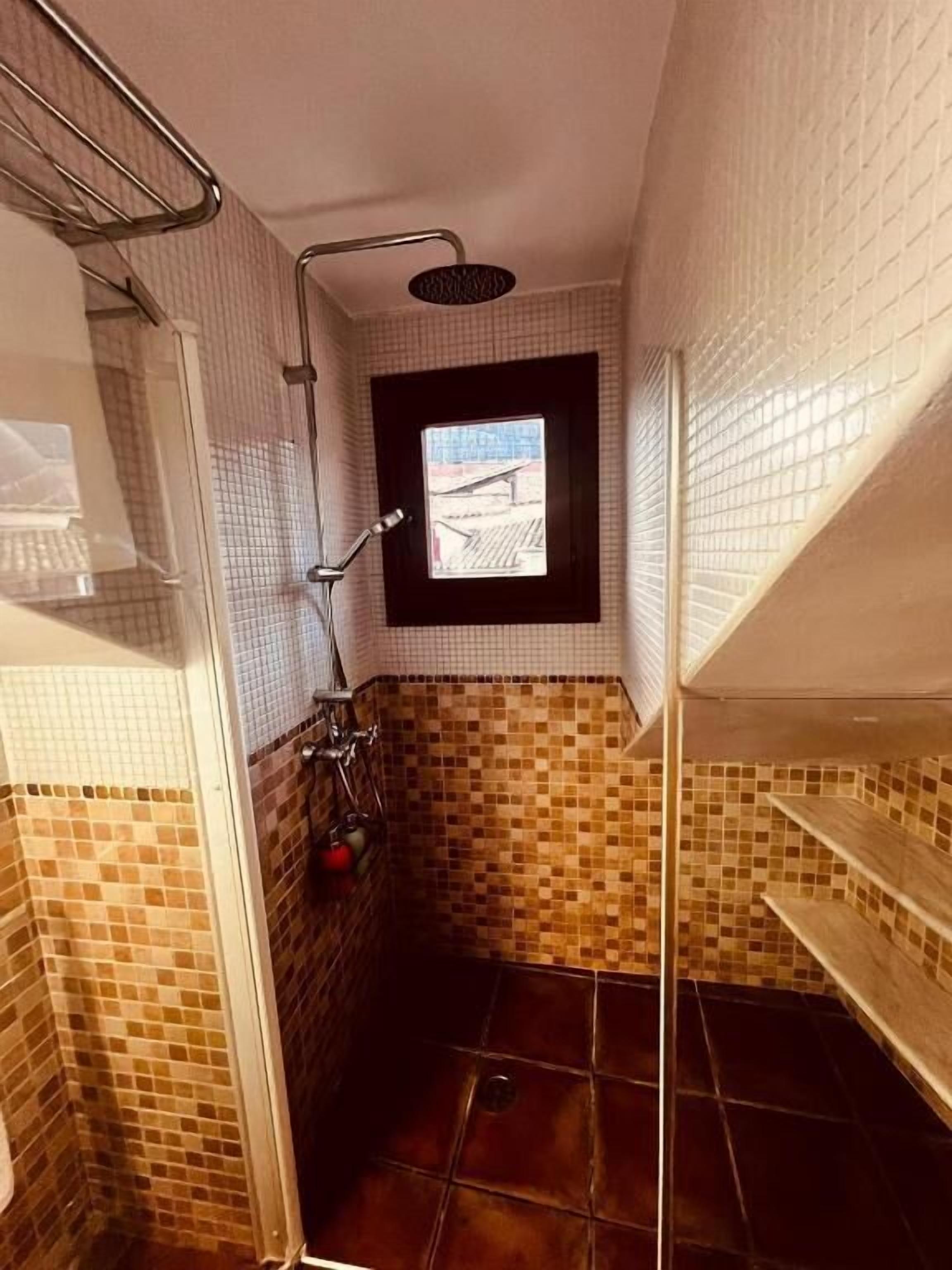 Un baño pequeño con ducha, ventana y paredes de azulejos.