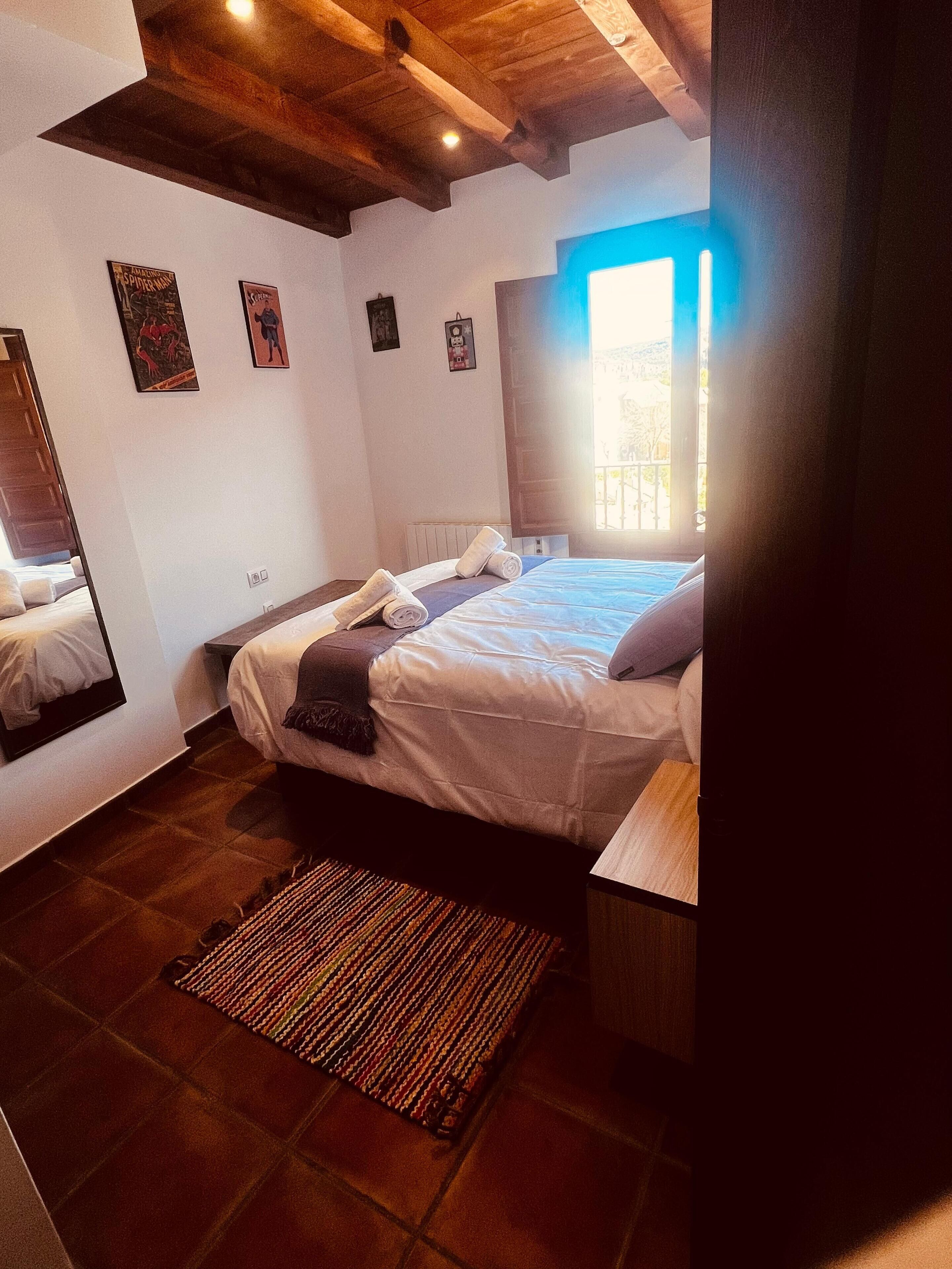 A bedroom with a bed, a wooden ceiling, a window, and a mirror.