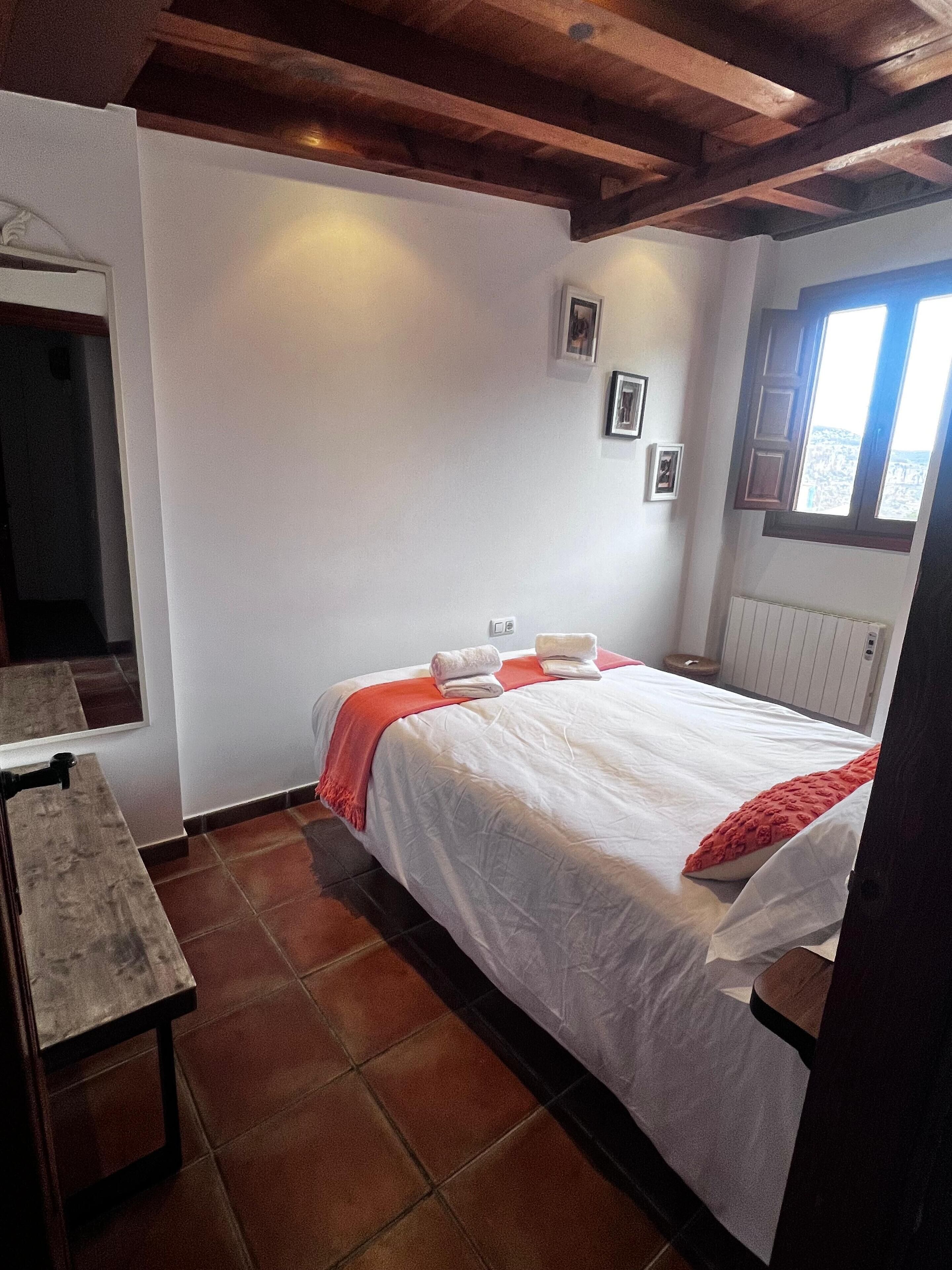 A bedroom with a bed, a wooden bench, a window, and a radiator.