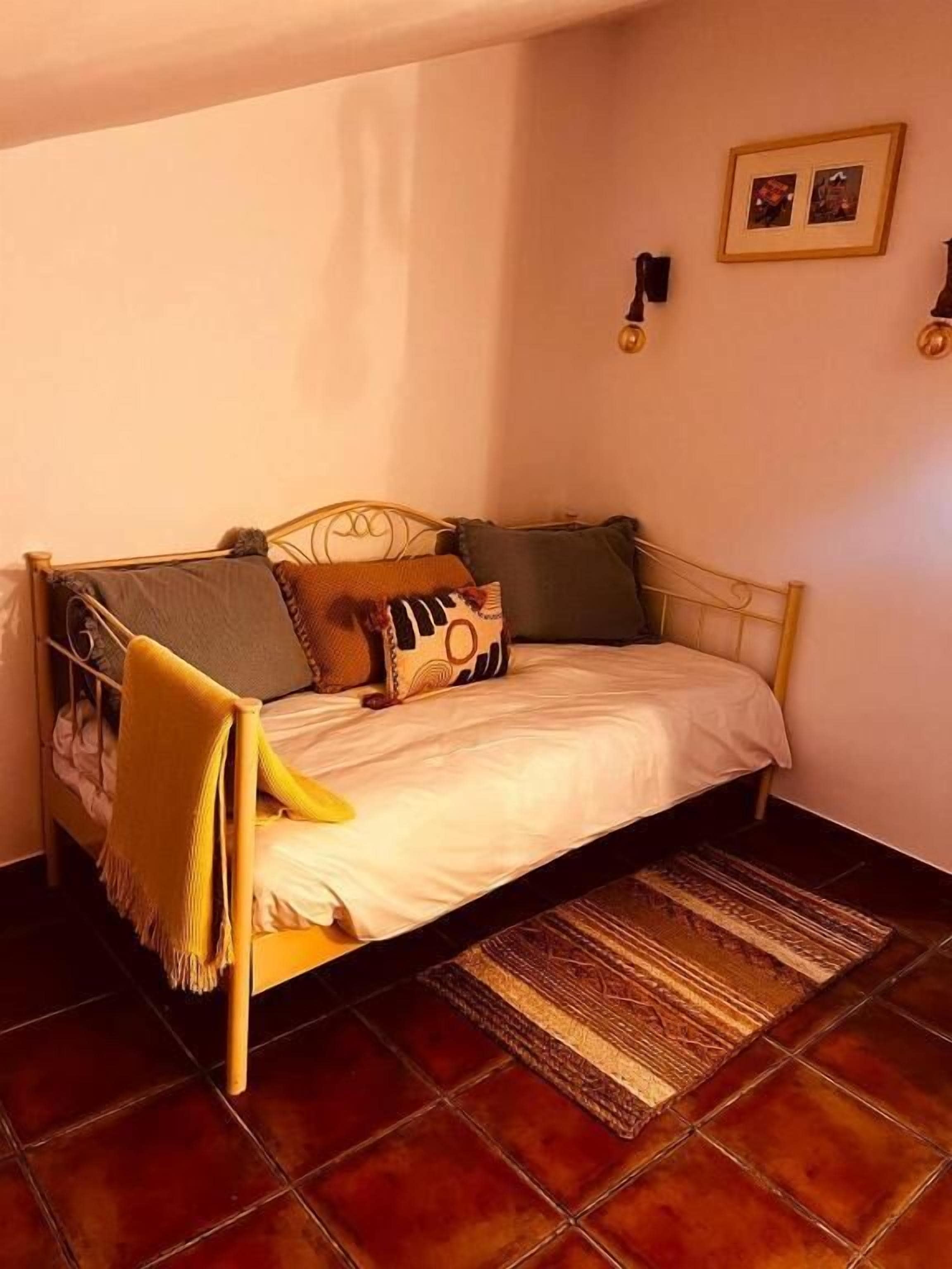 A single bed with a headboard, a throw blanket, and a patterned rug on a tiled floor.