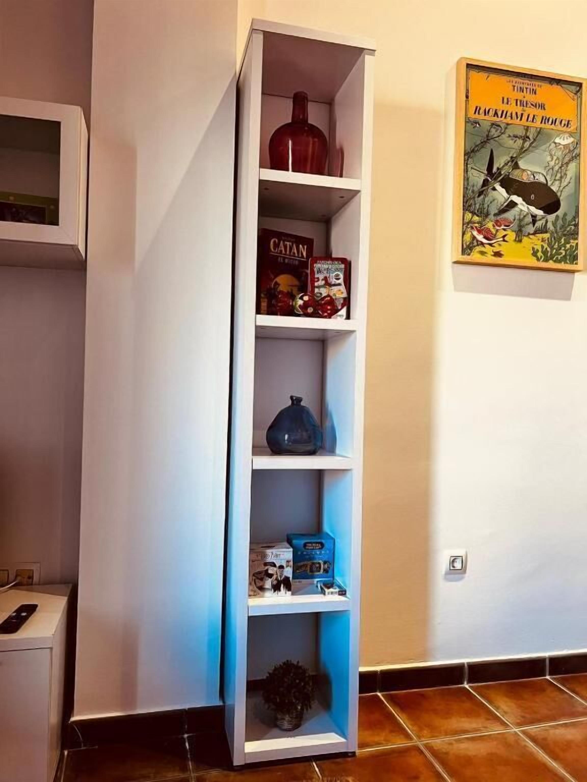 Une étagère blanche contenant divers objets, notamment un vase rouge, une boîte étiquetée « CATAN » et une boîte bleue.