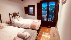 Une chambre avec deux lits, un banc en bois et une vue sur la ville par la fenêtre.