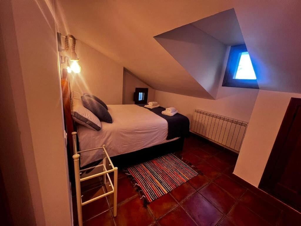 A bedroom with a bed, a small desk, a radiator, and a window.