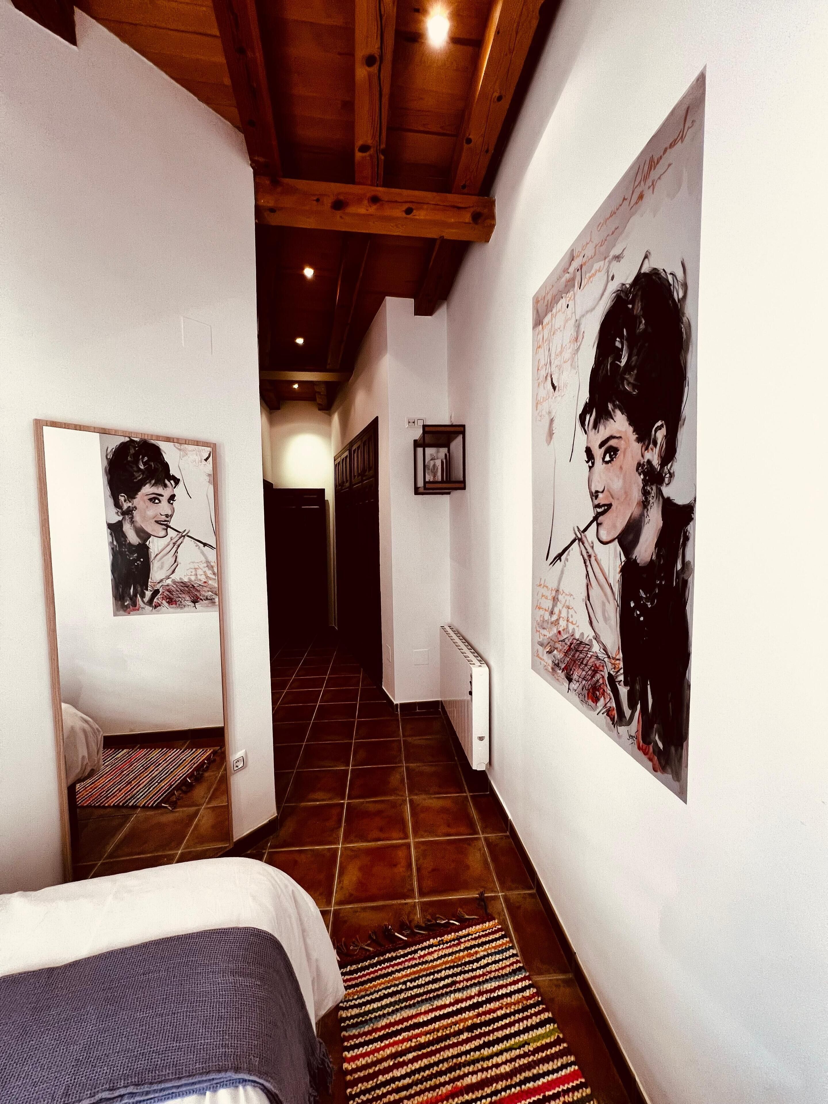 Un pasillo estrecho con una cama a la izquierda, un radiador y dos cuadros grandes en las paredes.