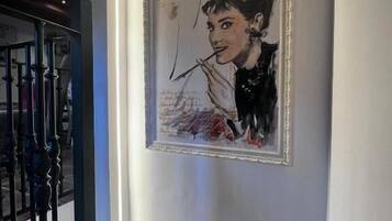 Et billede i ramme hænger på væggen i en gang med trappe og gelænder.