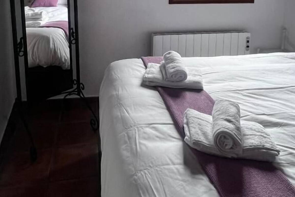 A bedroom with a bed, a large mirror, a window with shutters, and a radiator.