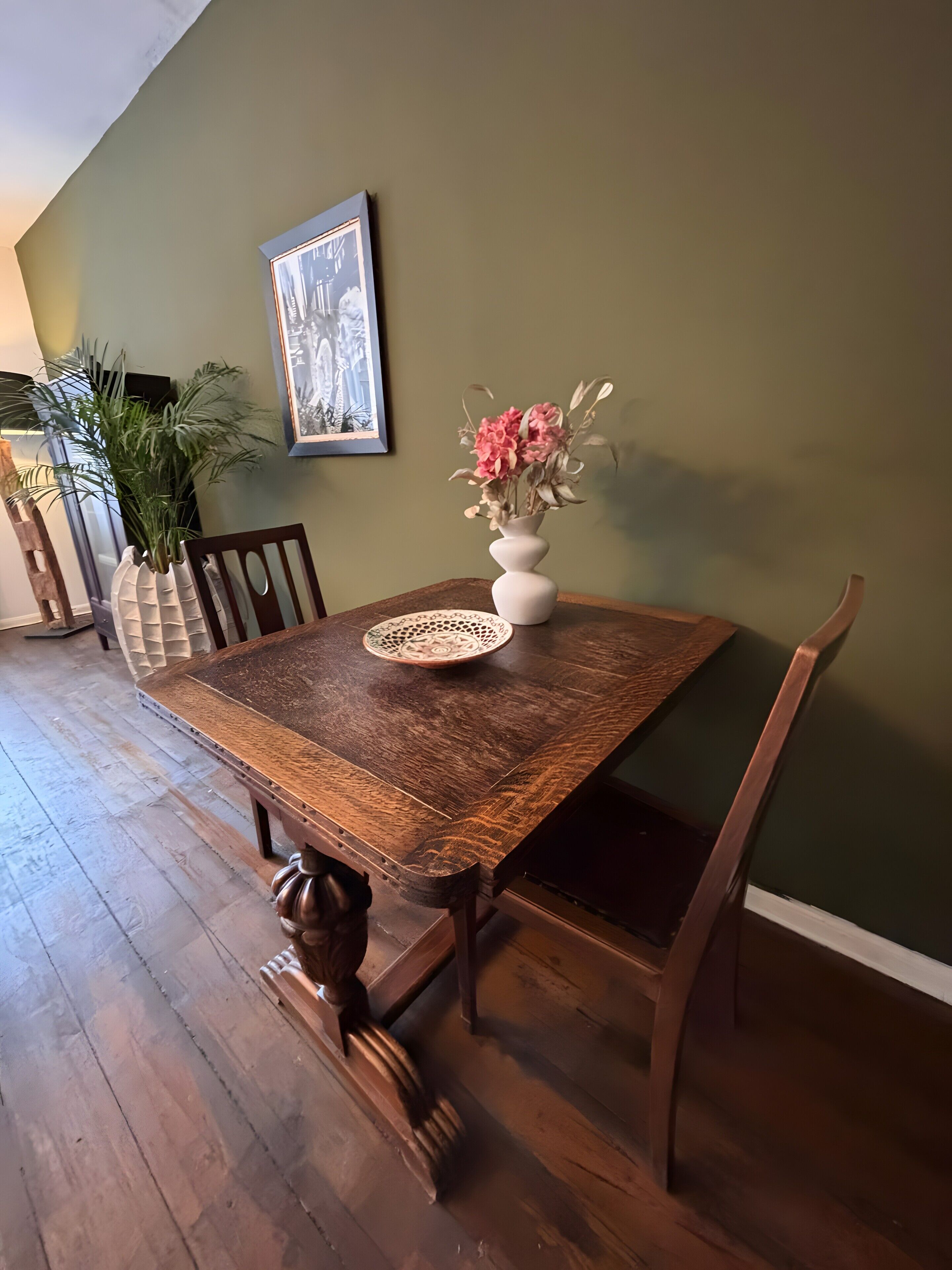 A dining table with chairs, a vase with flowers, a framed picture on the wall, and a plant.