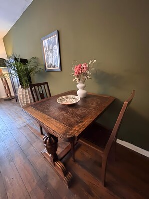 Une table à manger avec des chaises, un vase rempli de fleurs, un tableau encadré accroché au mur et une plante.