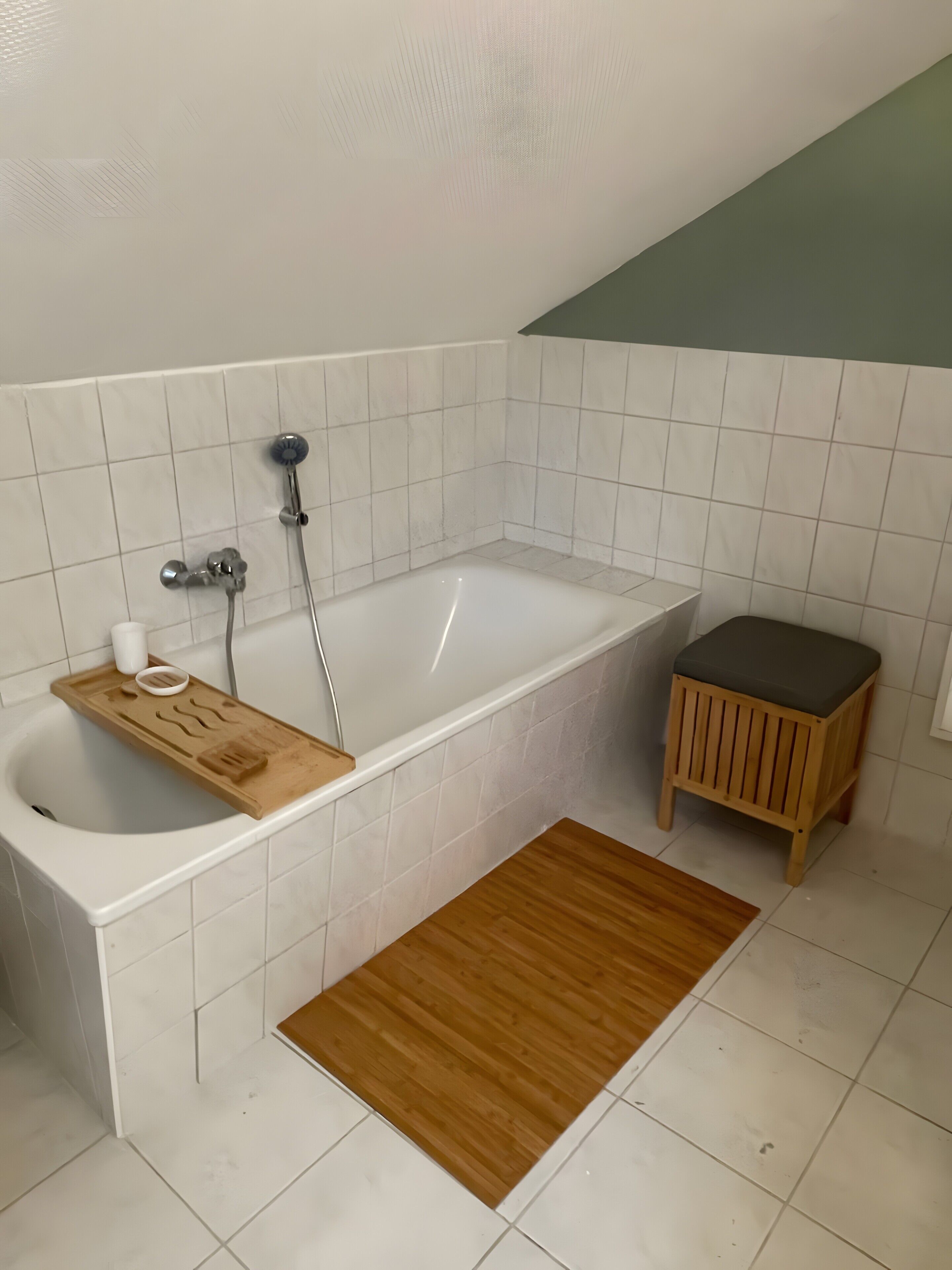 A bathroom with a bathtub, a wooden stool, a wooden tray, and a wooden mat.