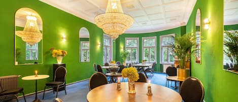 A room with green walls, a chandelier, and a round table with chairs.