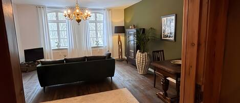 A spacious living room with a large sofa, a dining table, and a chandelier.