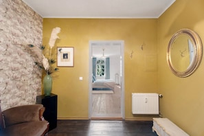 Una habitación con una pared amarilla, piso de madera, una fotografía enmarcada, un espejo y una silla.