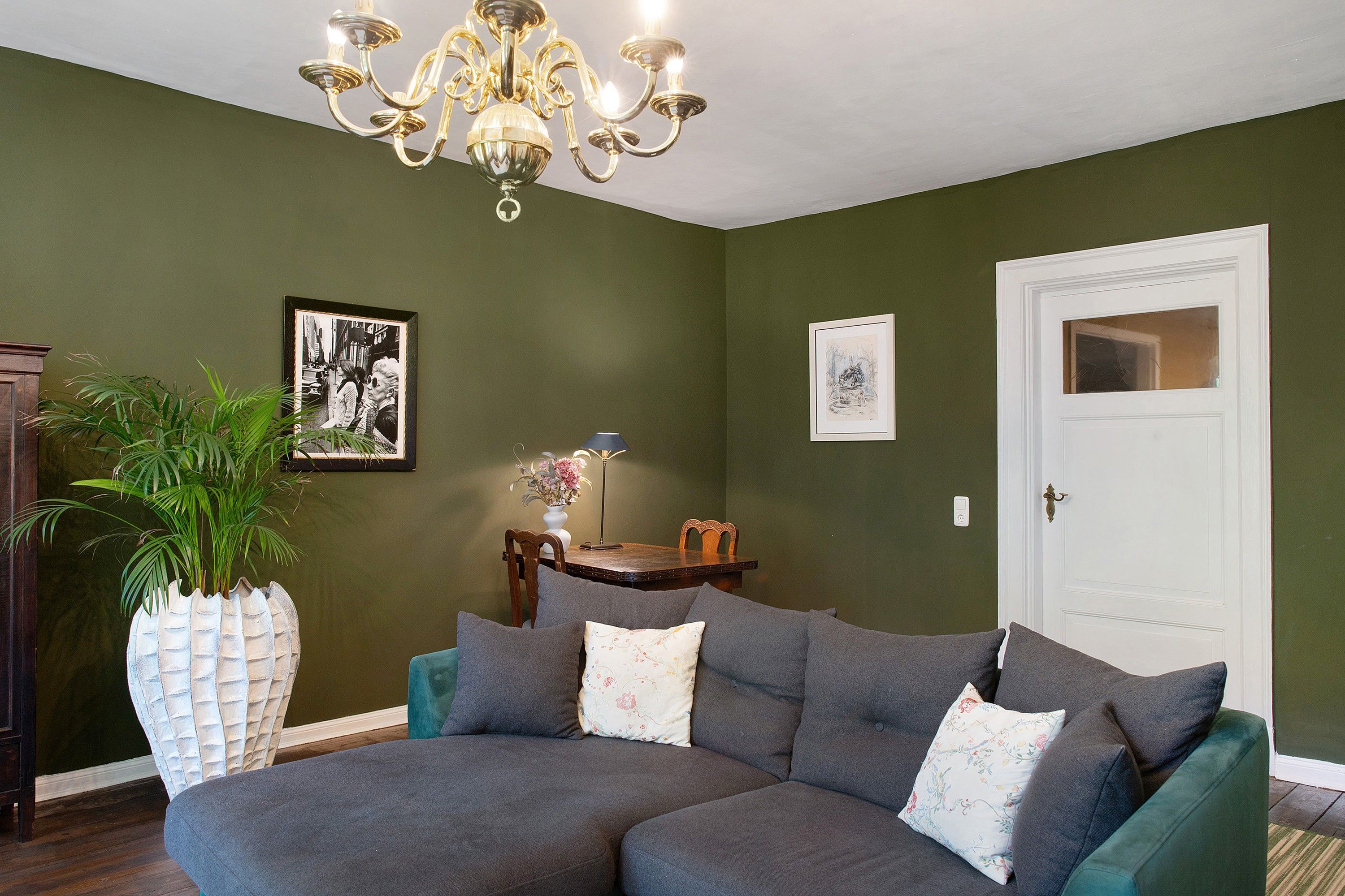 A living room with a sectional sofa, a potted plant, a lamp, and two framed pictures on the wall.