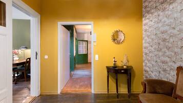 Una habitación con piso de madera, una puerta verde, un espejo y una pequeña mesa con una estatua.